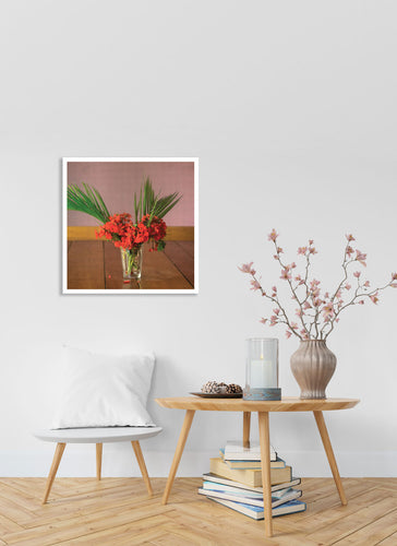 Flowers inside a glass in wooden table in front of a pink wall