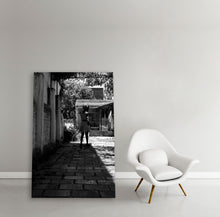 Load image into Gallery viewer, Frame with Black and white image of migrant woman walking in her courtyard in the shadows
